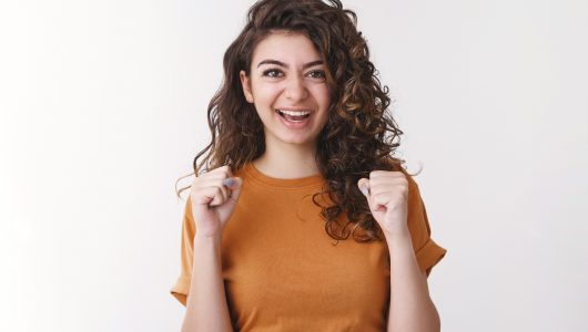 Yes lucky me. Happy triumphing young joyful armenian woman curly-haired clench fists celebrating successful win lottery smiling say yeah, excited good positive result, standing white background.